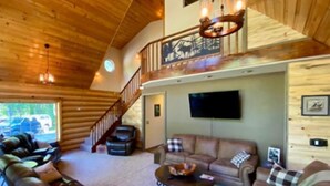 Un vaste espace de vie doté d’un haut plafond, d’un escalier menant à l’étage supérieur, d’un téléviseur à écran plat fixé au mur et d’un ensemble de canapés en cuir.