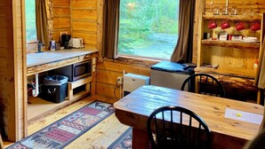 L’intérieur chaleureux d’un chalet, avec un revêtement mural en bois, une table à manger, des chaises, un coin cuisine équipé d’un four à micro-ondes et d’un réfrigérateur, ainsi qu’une fenêtre agrémentée de rideaux.