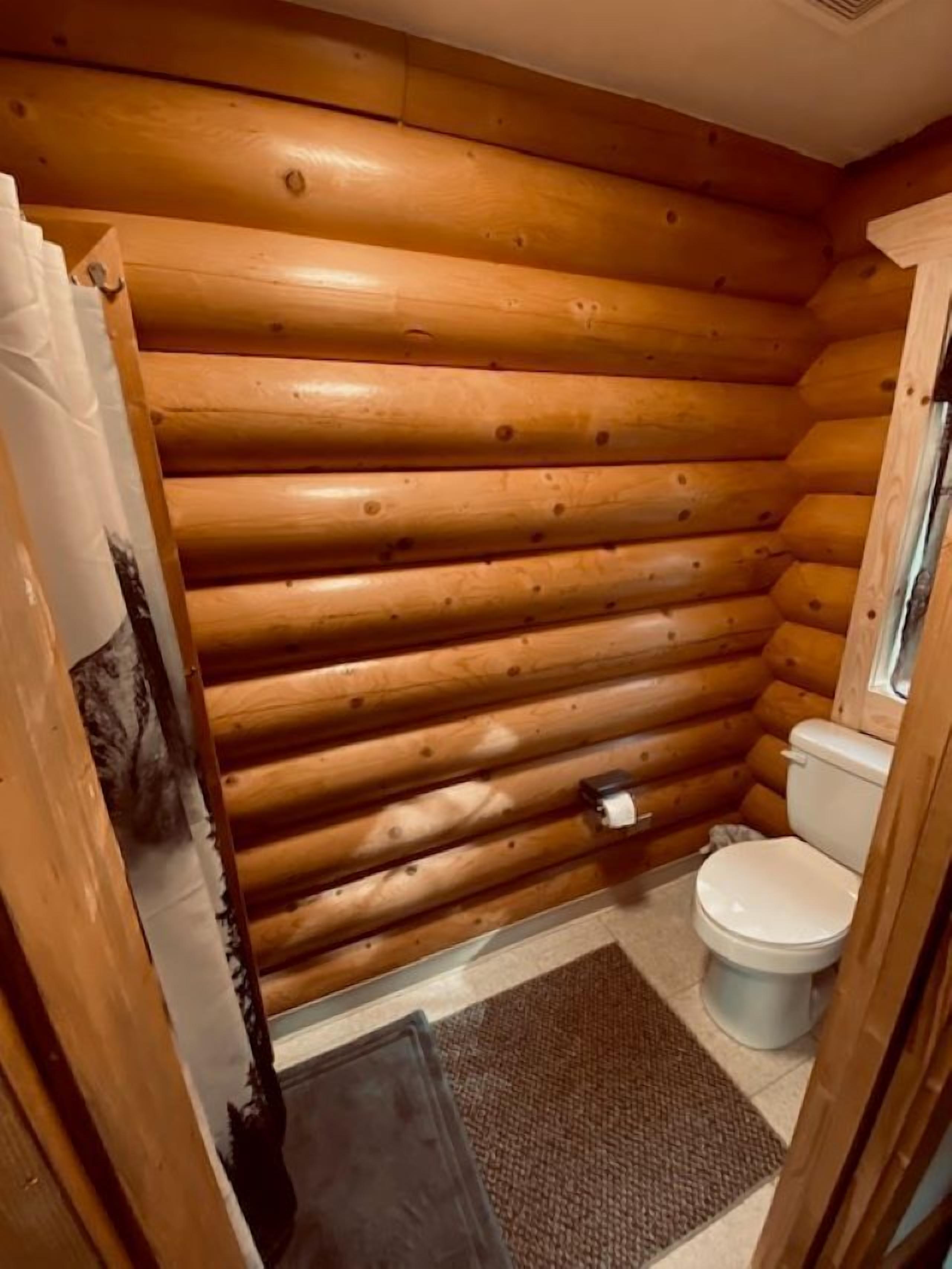 Un baño de estilo cabaña de madera con inodoro, zona de ducha y una alfombra en el suelo.