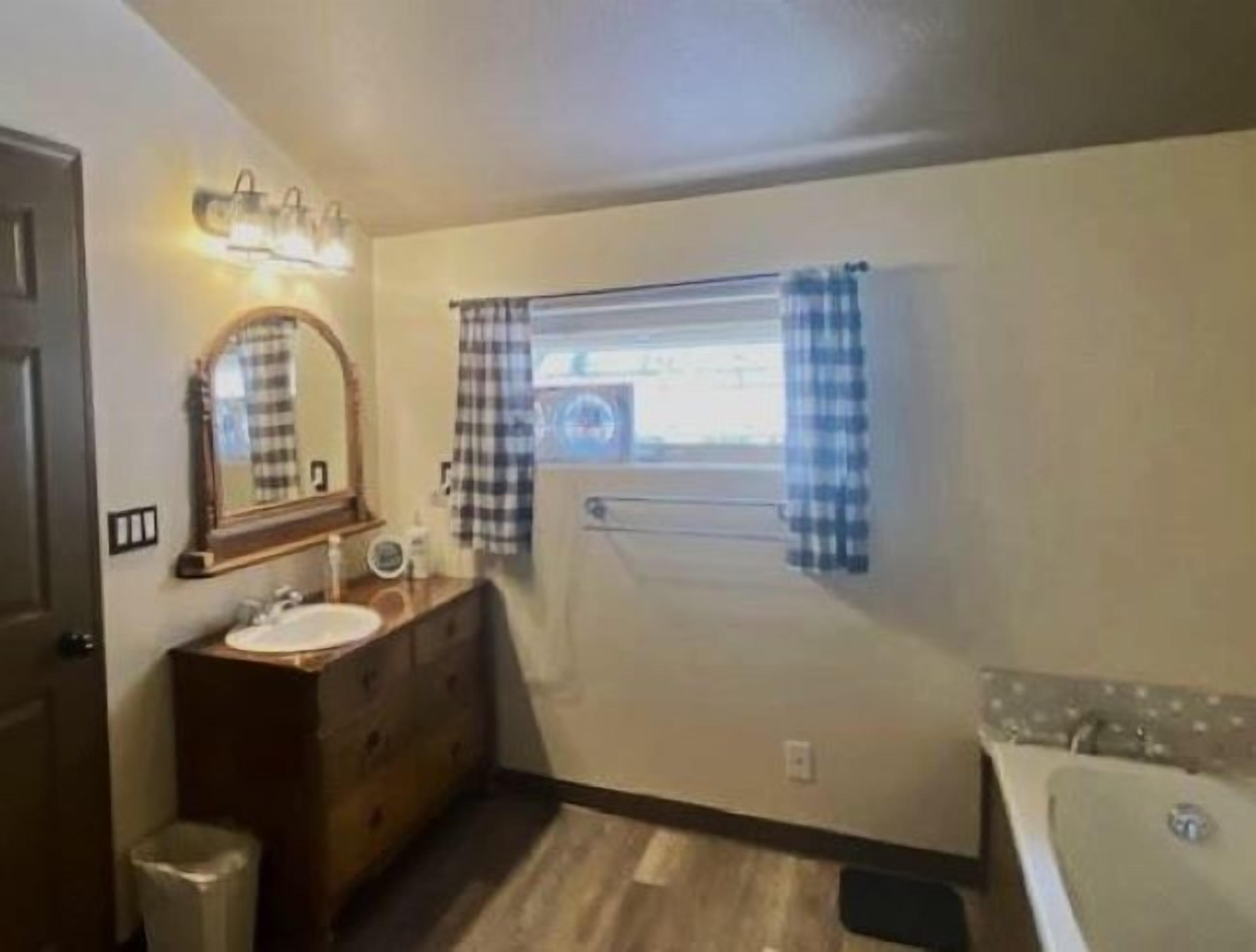 Un baño pequeño y funcional con tocador de madera, espejo, lavamanos y bañera.