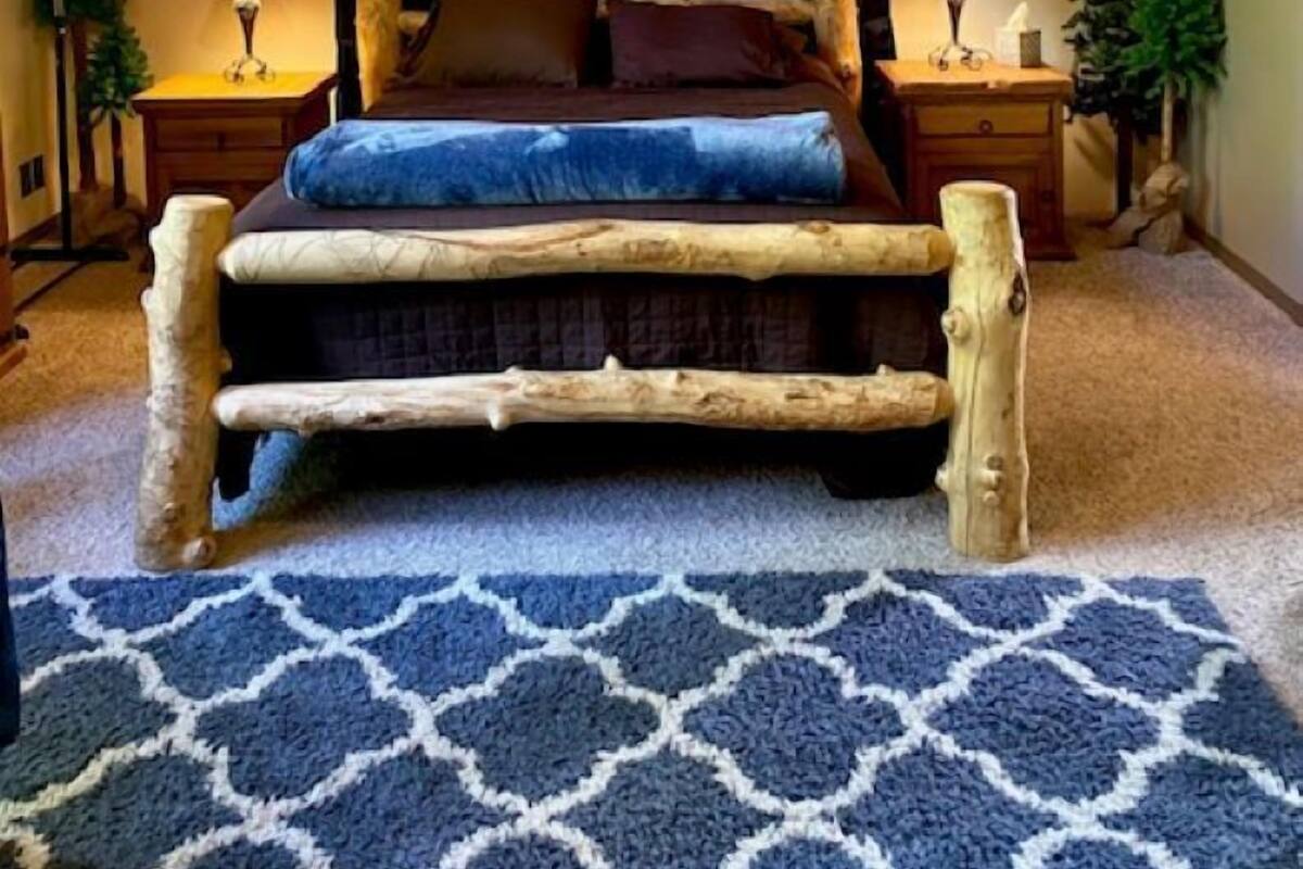 A rustic wooden bed with a slatted headboard, a blue patterned rug, and a ceiling fan.
