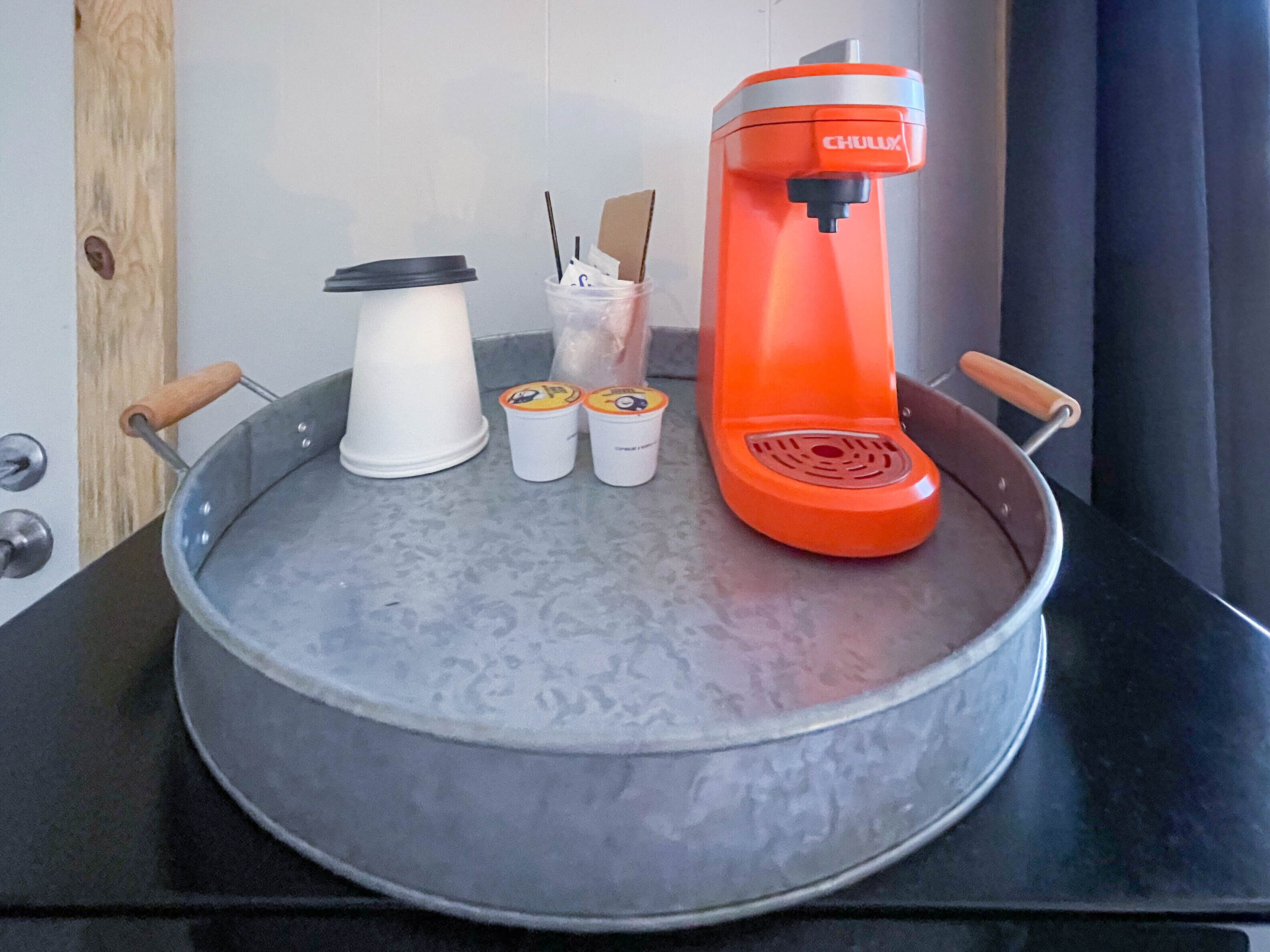 Una cafetera, una taza blanca y dos tazas pequeñas sobre una encimera.