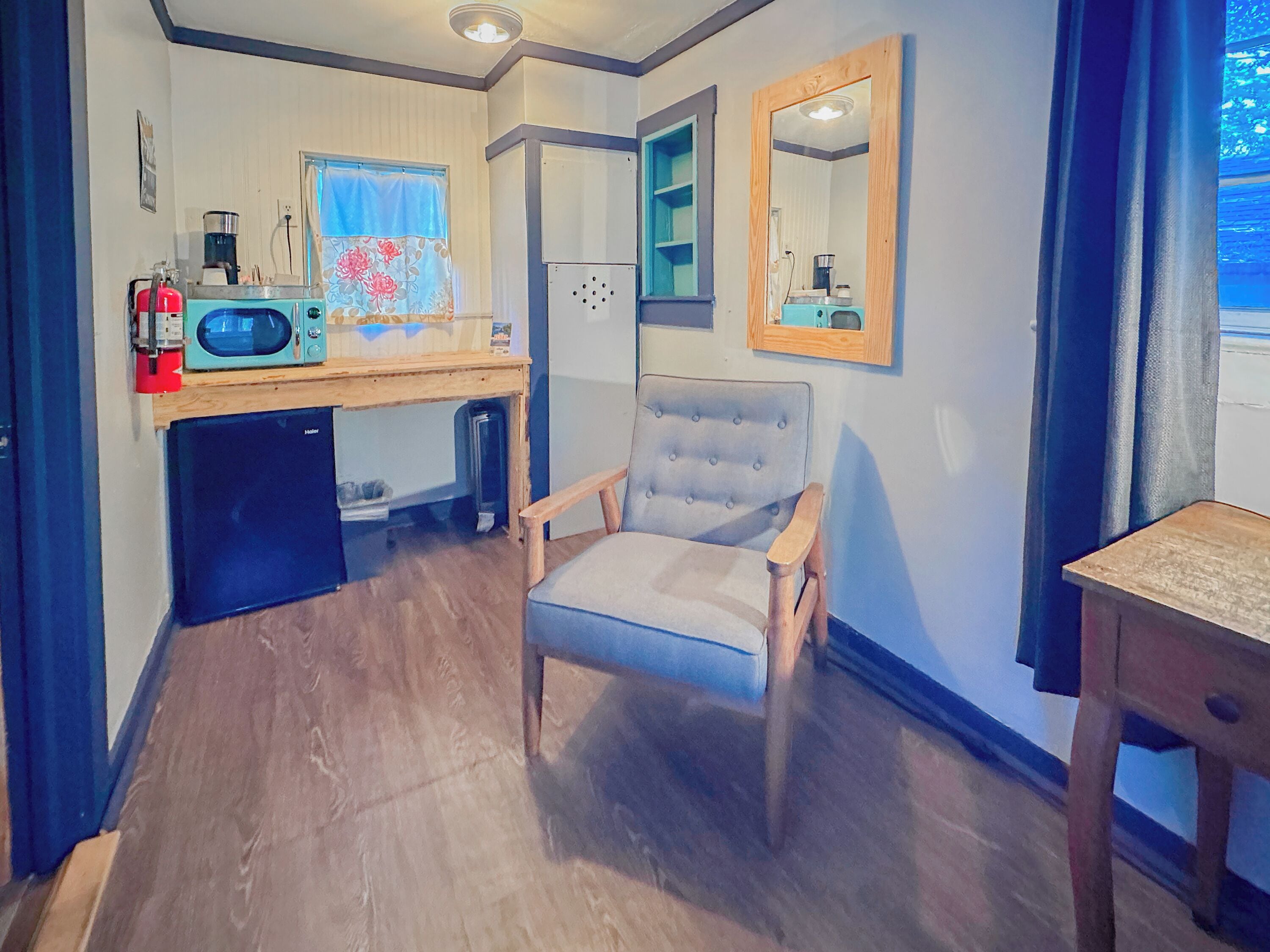 A compact room with a kitchenette, a chair, a small table, and a mirror.
