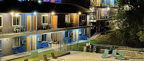 A two-story building with a swimming pool, outdoor seating, and a well-lit exterior.