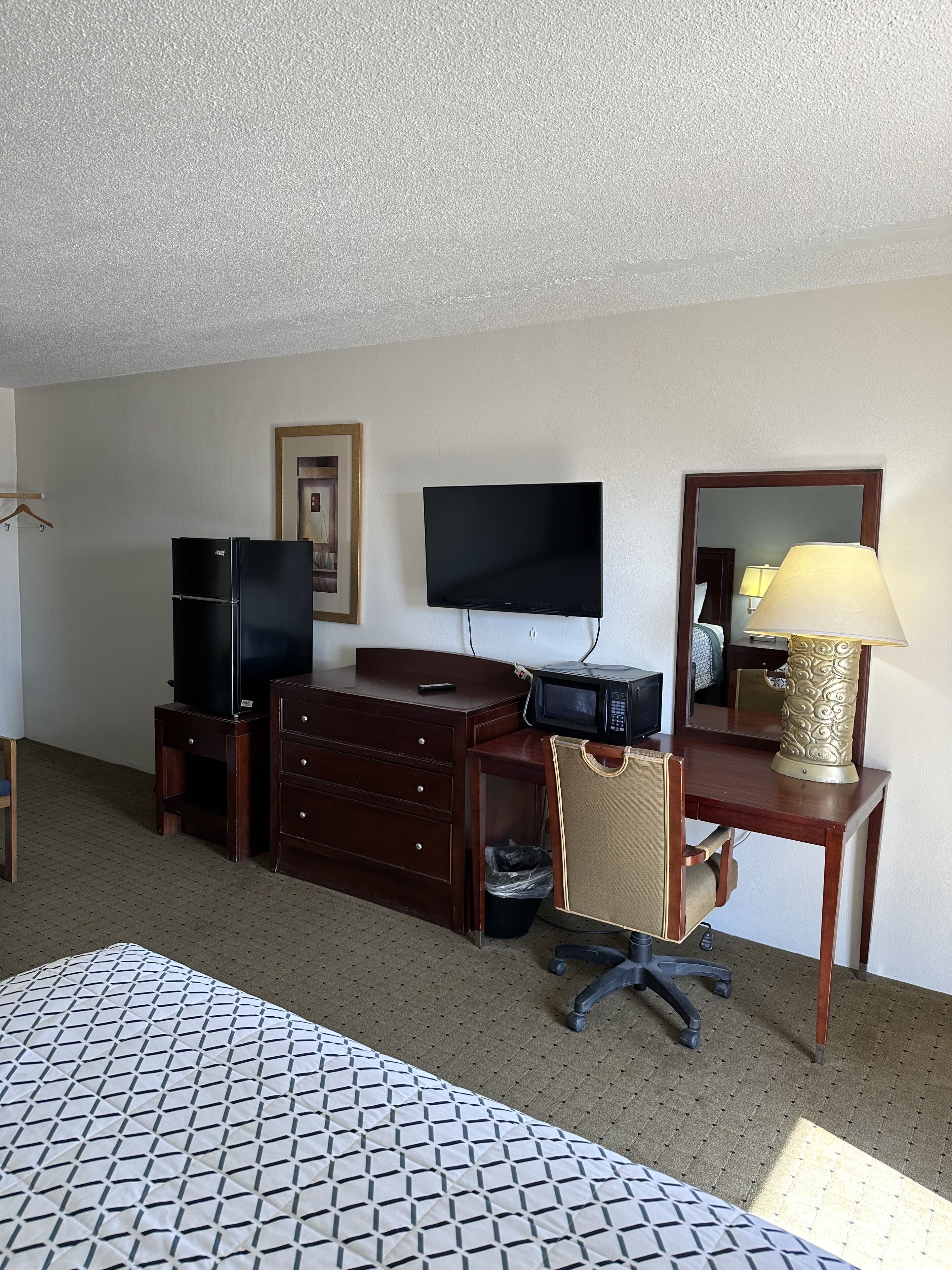 A hotel room with a bed, a desk with a computer, a television, a dresser, and a lamp.