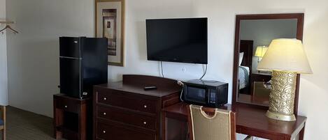 A hotel room with a bed, a desk with a computer, a television, a dresser, and a lamp.