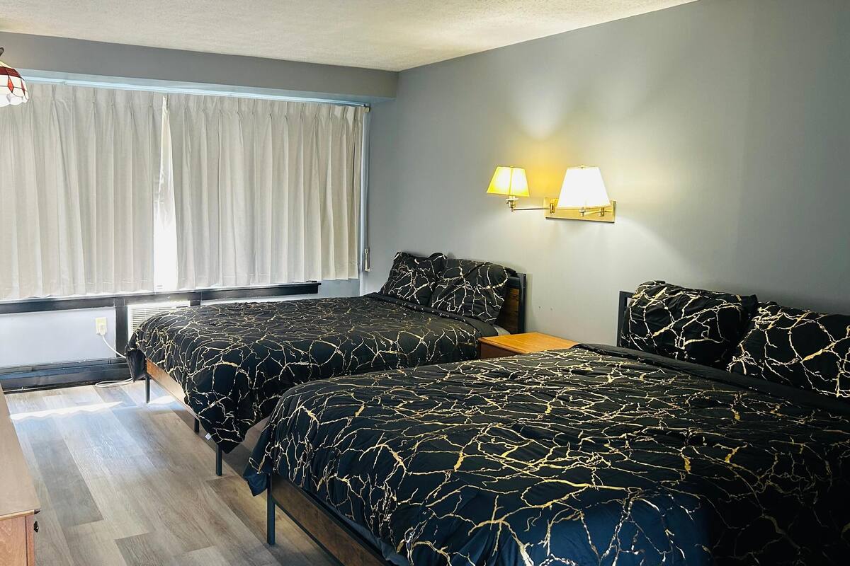 A hotel room with two beds, a desk, a chair, a television, and a window with curtains.