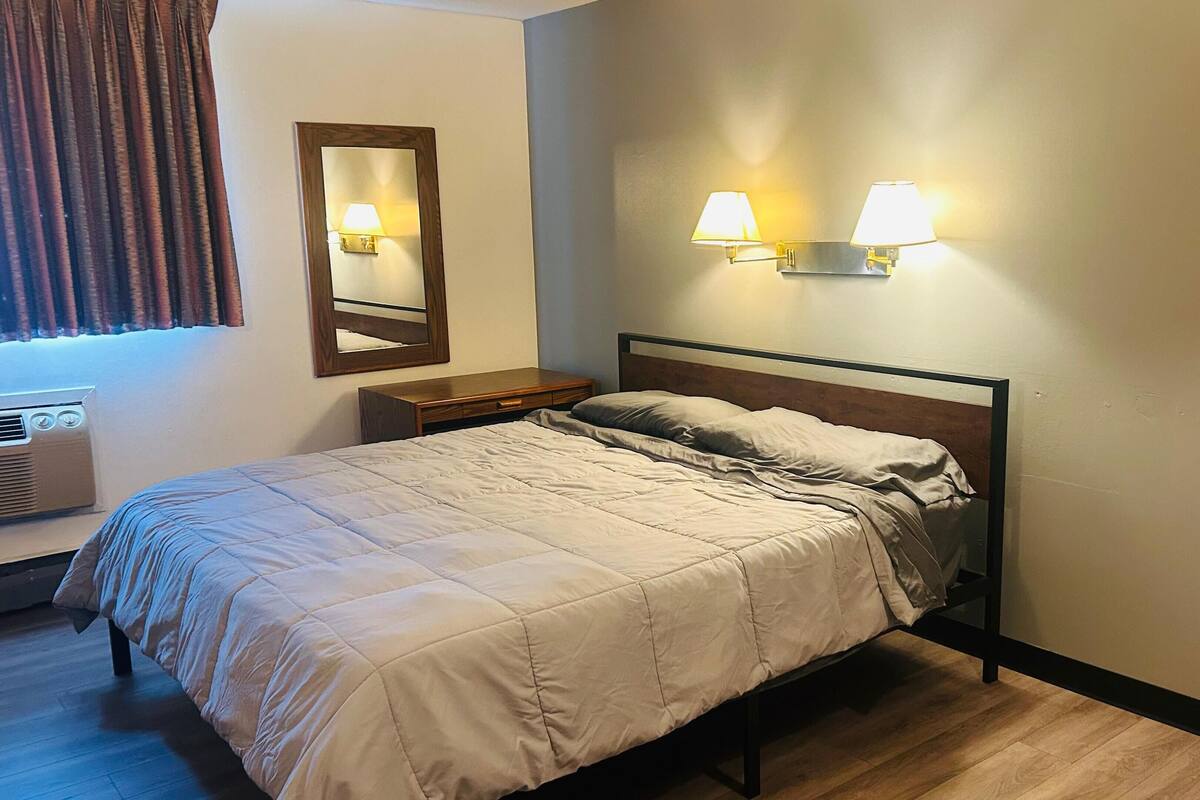 A neatly made bed with a wooden headboard, a bedside table, and two wall-mounted lamps.