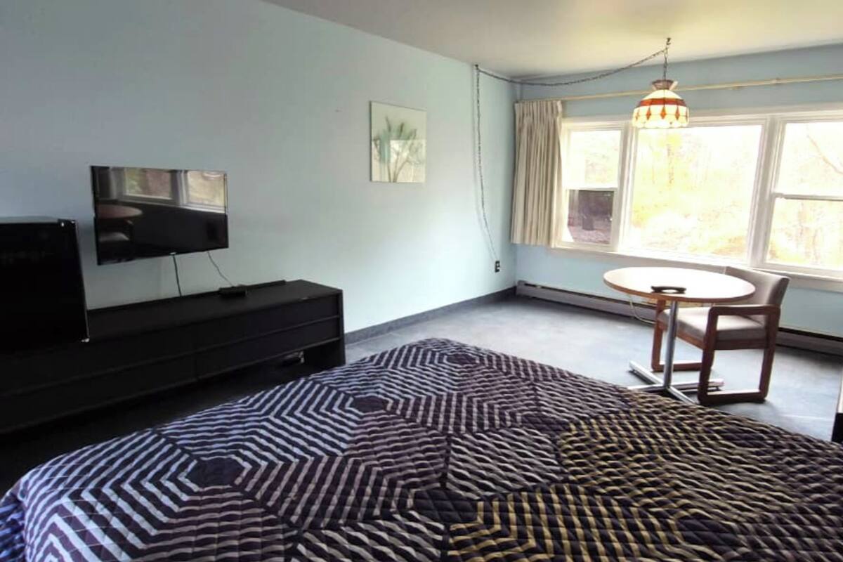 A bedroom with a bed, a TV, a small table, and a chair.