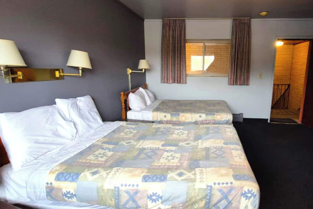 A hotel room with two beds, a window with curtains, and wall-mounted lamps.