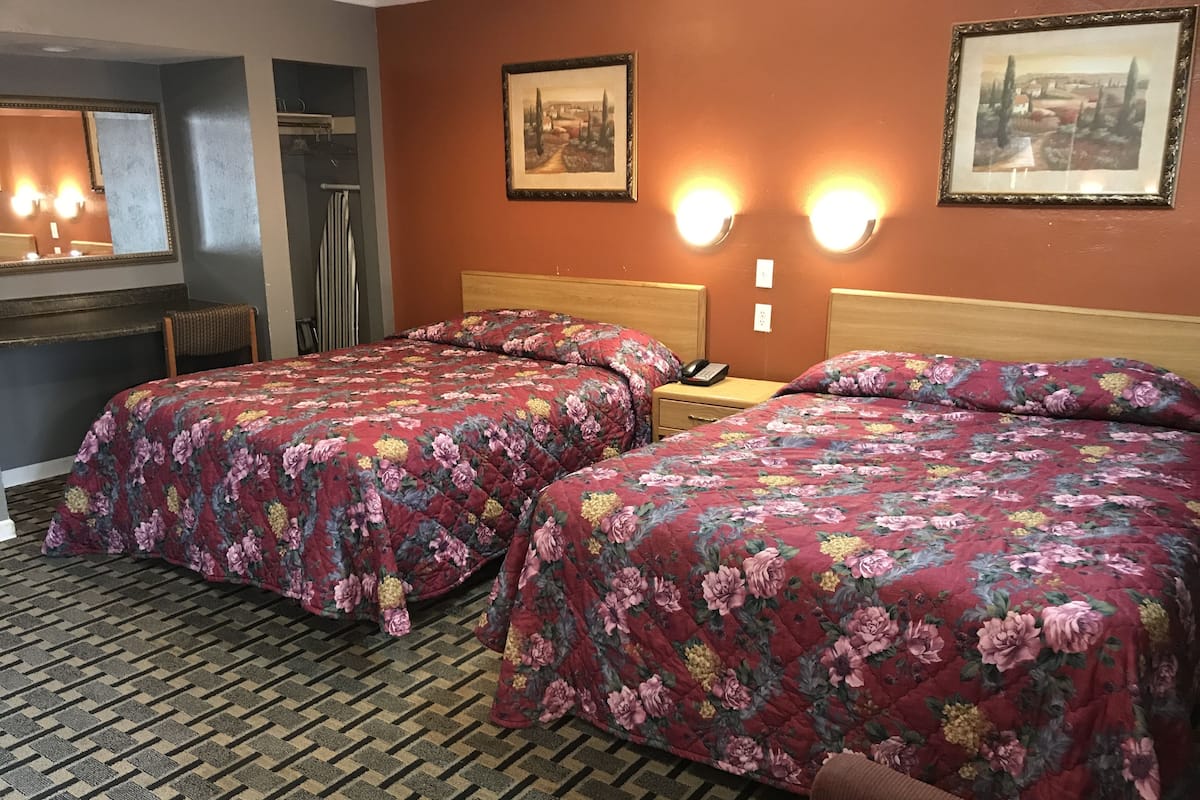 A hotel room with two beds, a wooden headboard, a nightstand with a phone, and a mirror.