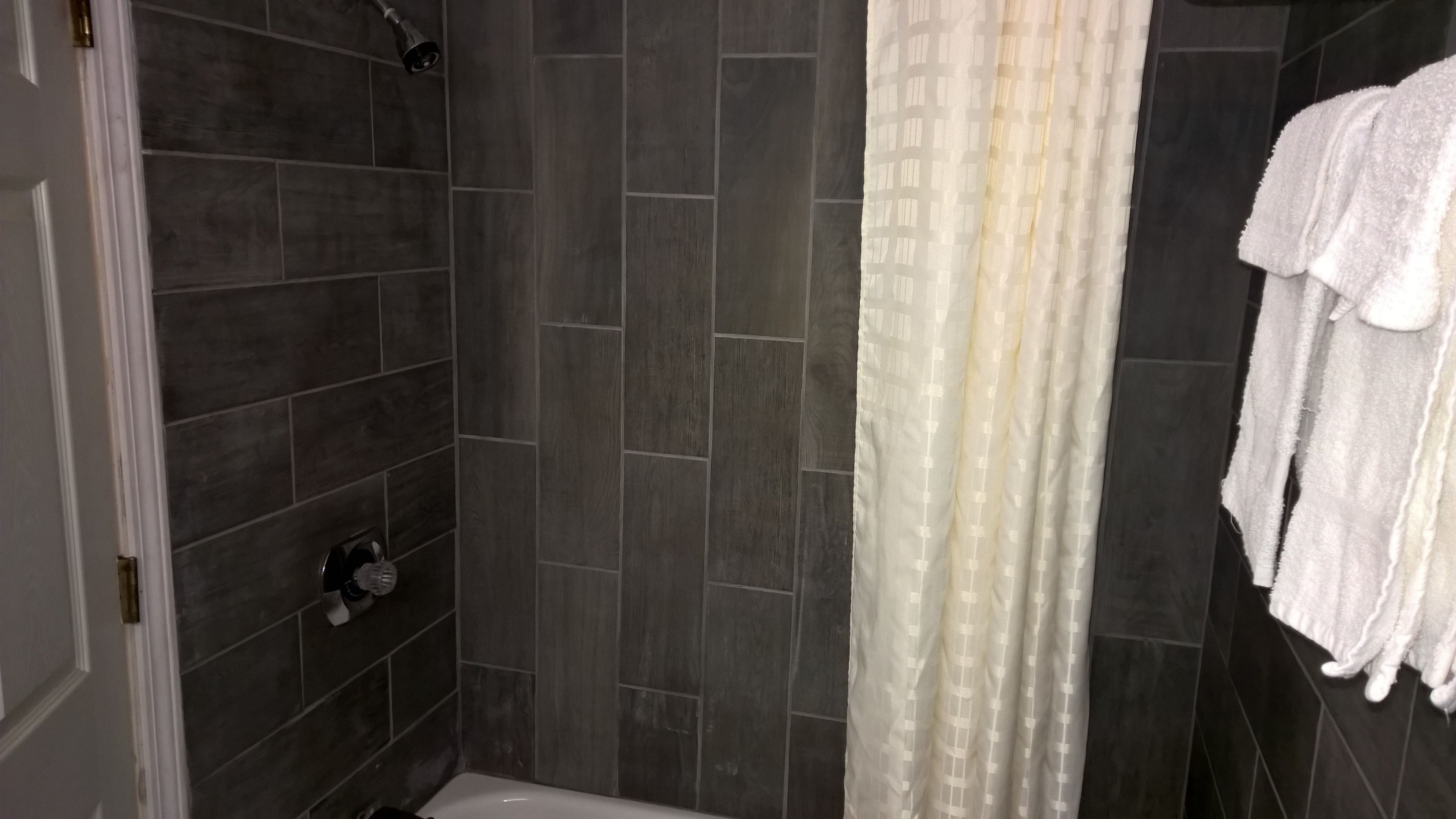 A shower area with dark tiled walls, a white shower curtain, and a white towel hanging on the wall.