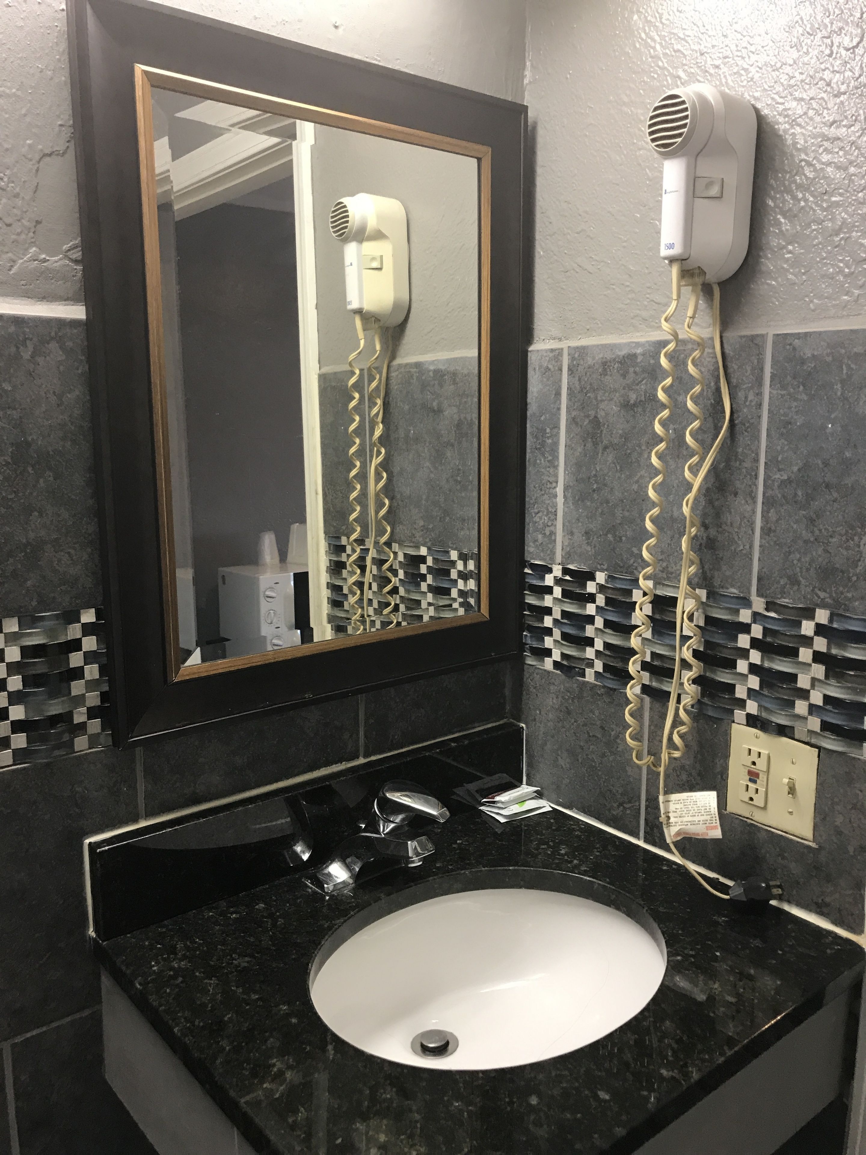 A bathroom with a black sink, a mirror with a wooden frame, and a hairdryer mounted on the wall.
