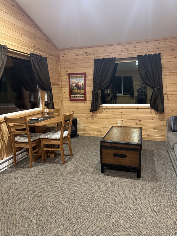 Un interior de madera con una mesa de comedor y sillas, una pequeña mesa de madera y un cartel en la pared.