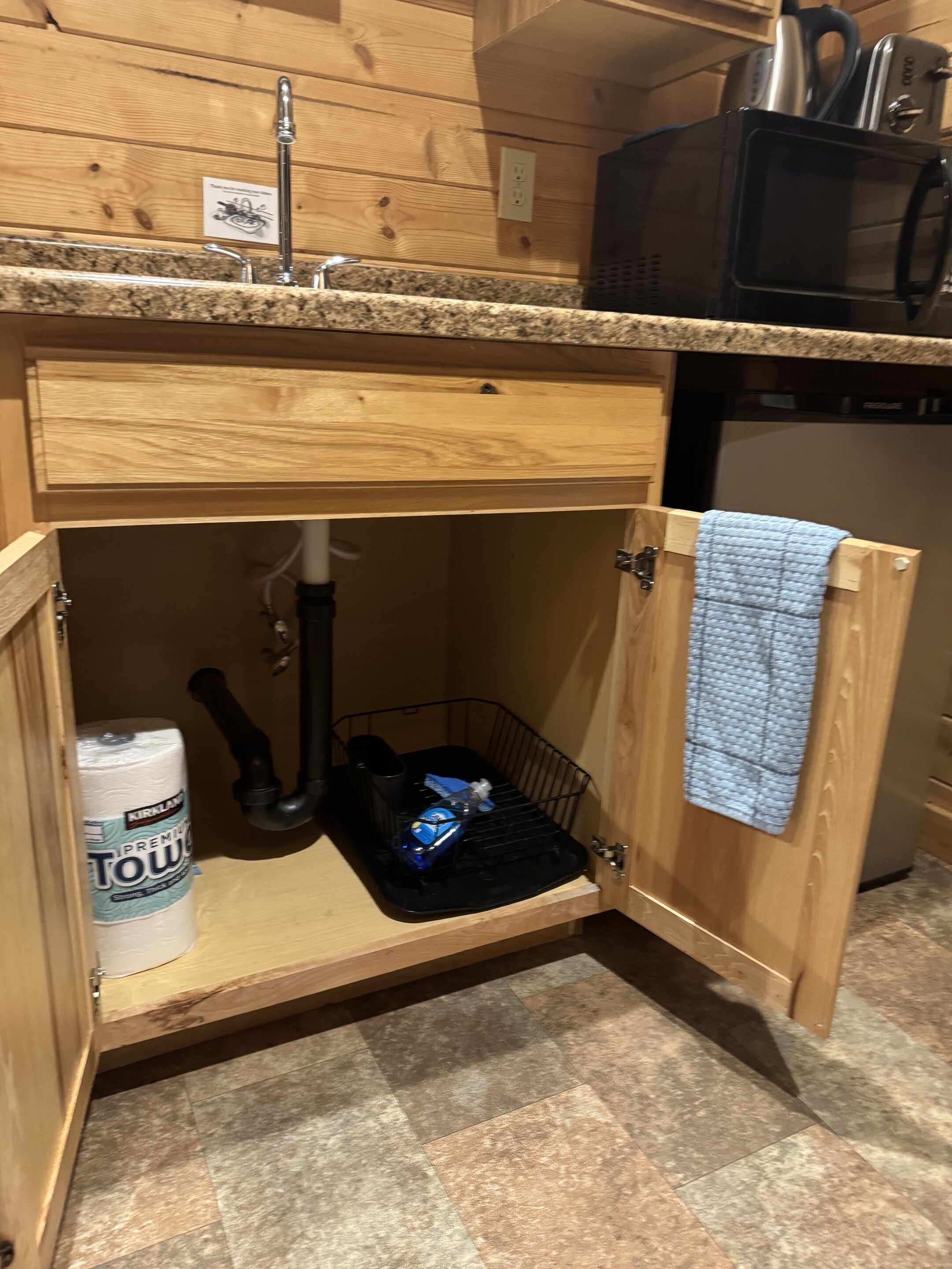Una cocina con encimera de madera, un lavabo, un microondas negro y un armario de almacenamiento con una toalla colgada en la puerta.