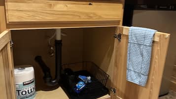 Una cocina con encimera de madera, un lavabo, un microondas negro y un armario de almacenamiento con una toalla colgada en la puerta.