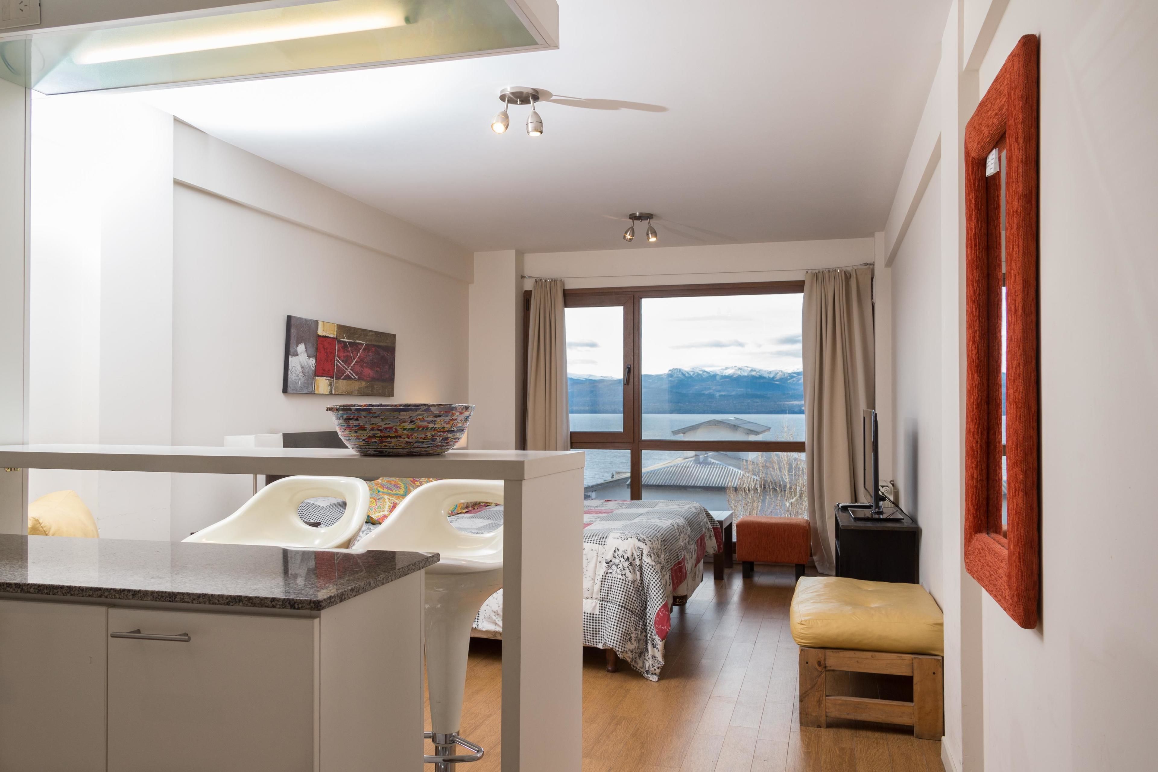 A modern room with a kitchen area, a dining table, a large window with a view, and a bed with a view.