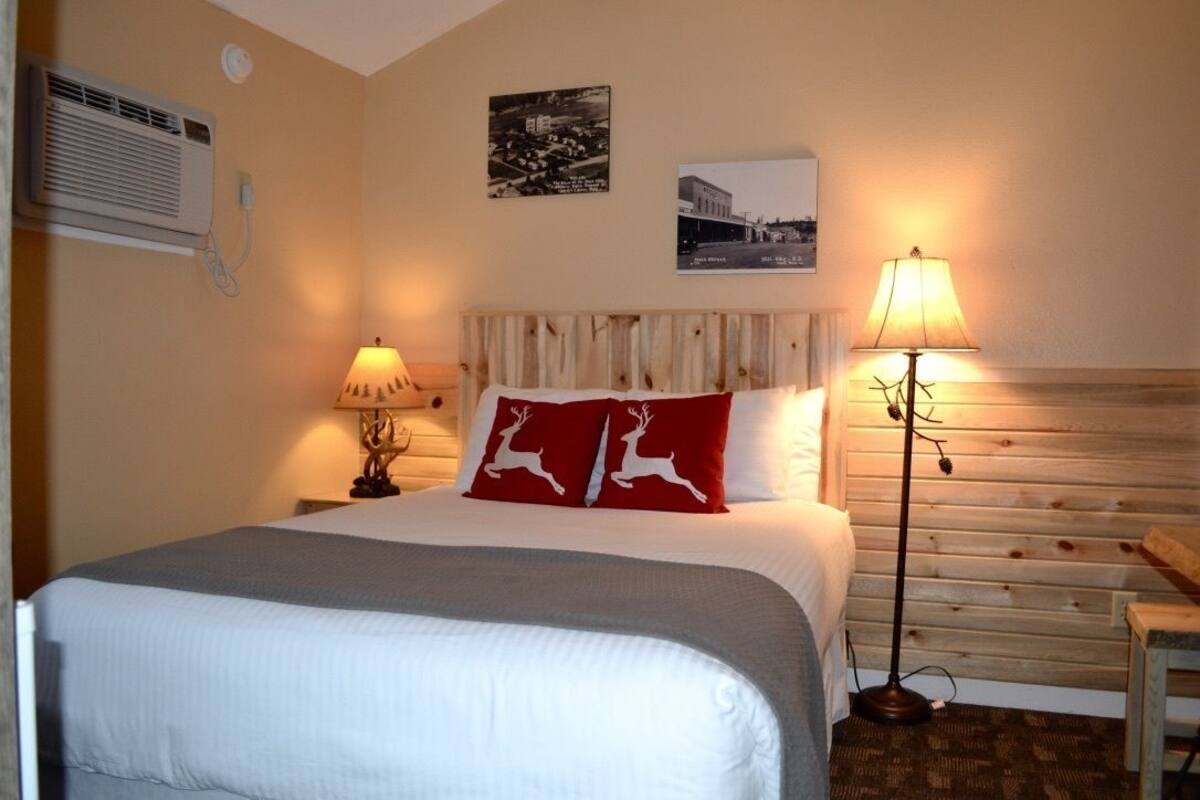 Een keurig opgeruimde hotelkamer met een bed, twee bedlampen en een luchtverkoeler aan de muur.