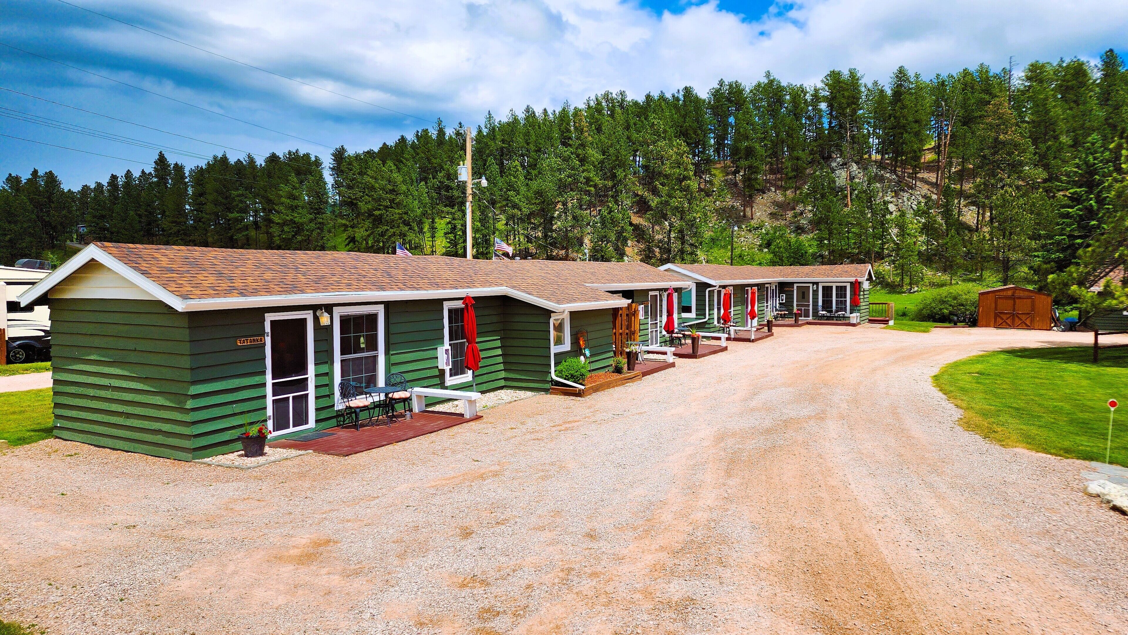 A row of green cabins with a gravel driveway, surrounded by trees.
