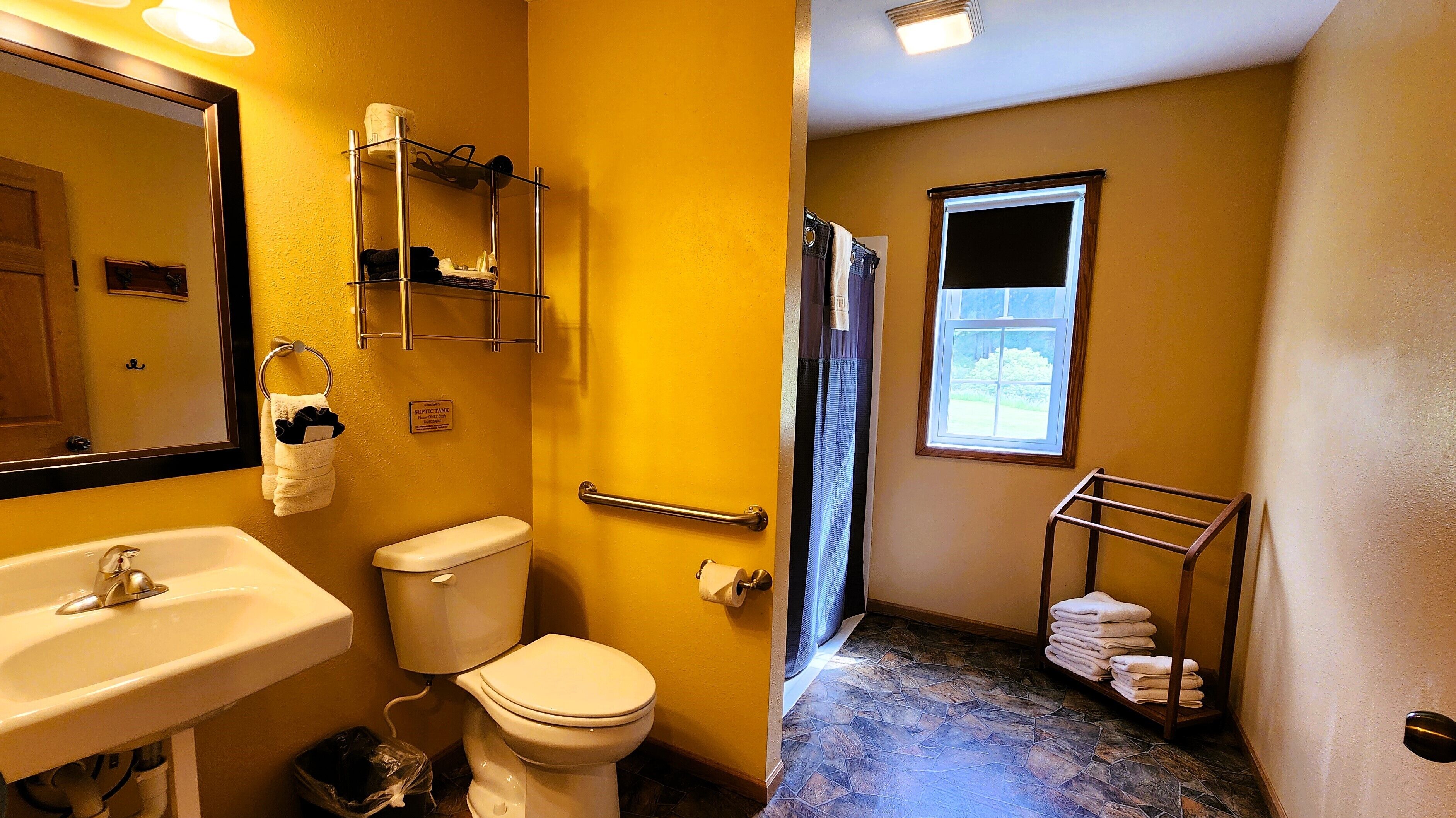 A bathroom with a sink, toilet, and shower. There is a towel rack with towels, a toilet paper holder, and a sign indicating a septic tank.
