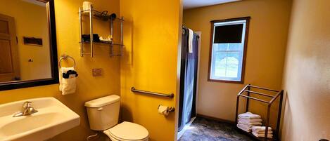 A bathroom with a sink, toilet, and shower. There is a towel rack with towels, a toilet paper holder, and a sign indicating a septic tank.