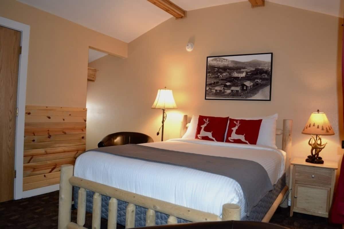 Een slaapkamer met een bed, twee bedlampen, een stoel, een houten hoofdbord, een nachtkastje en een ingelijste foto aan de muur.