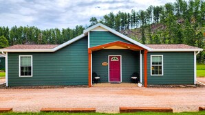 A two-story building with a green exterior, a red door, and a small porch area. - Black Elk Resort Cottages and RV Park (Hill City)