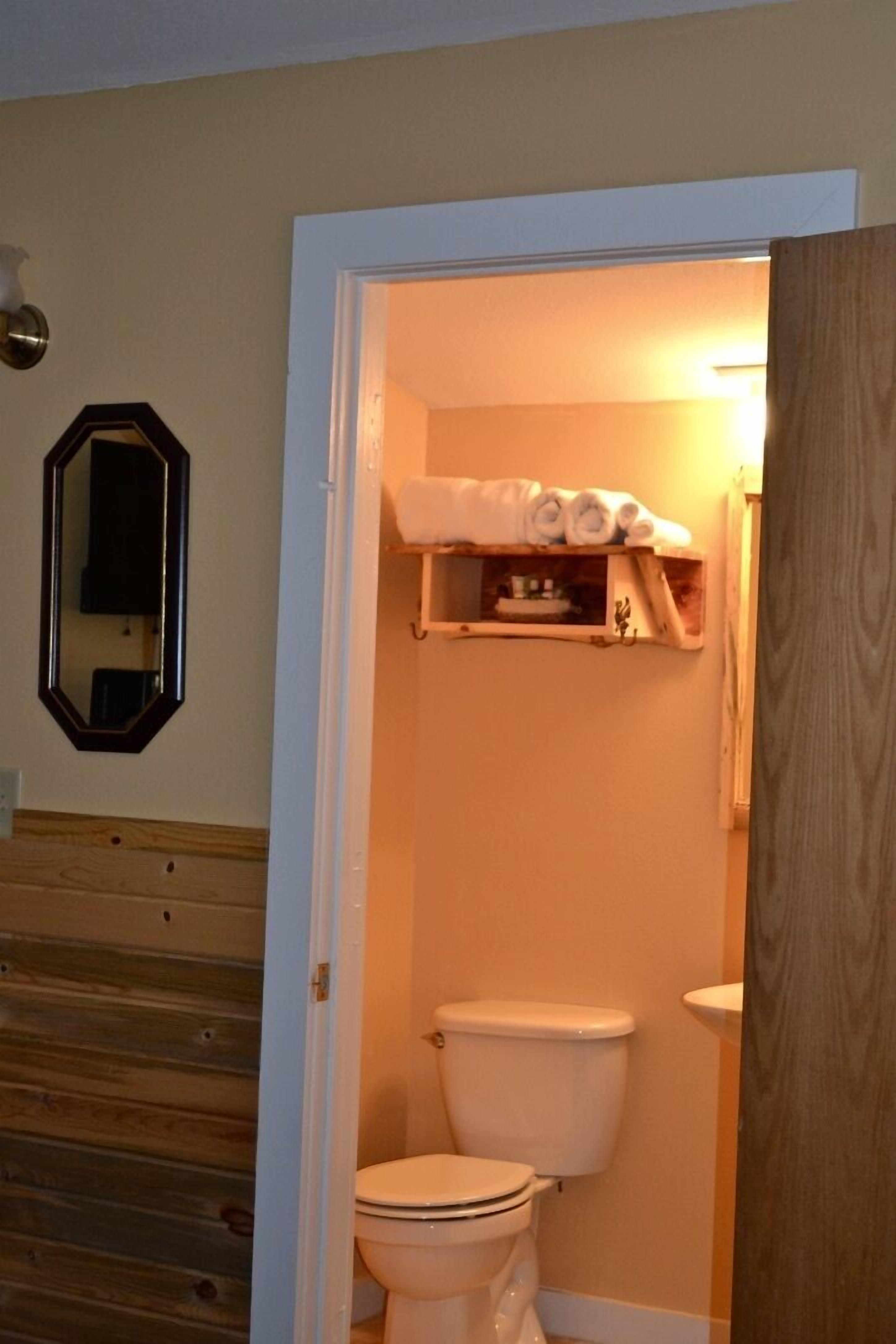 A bathroom with a toilet, a shelf with towels, and a mirror on the wall.