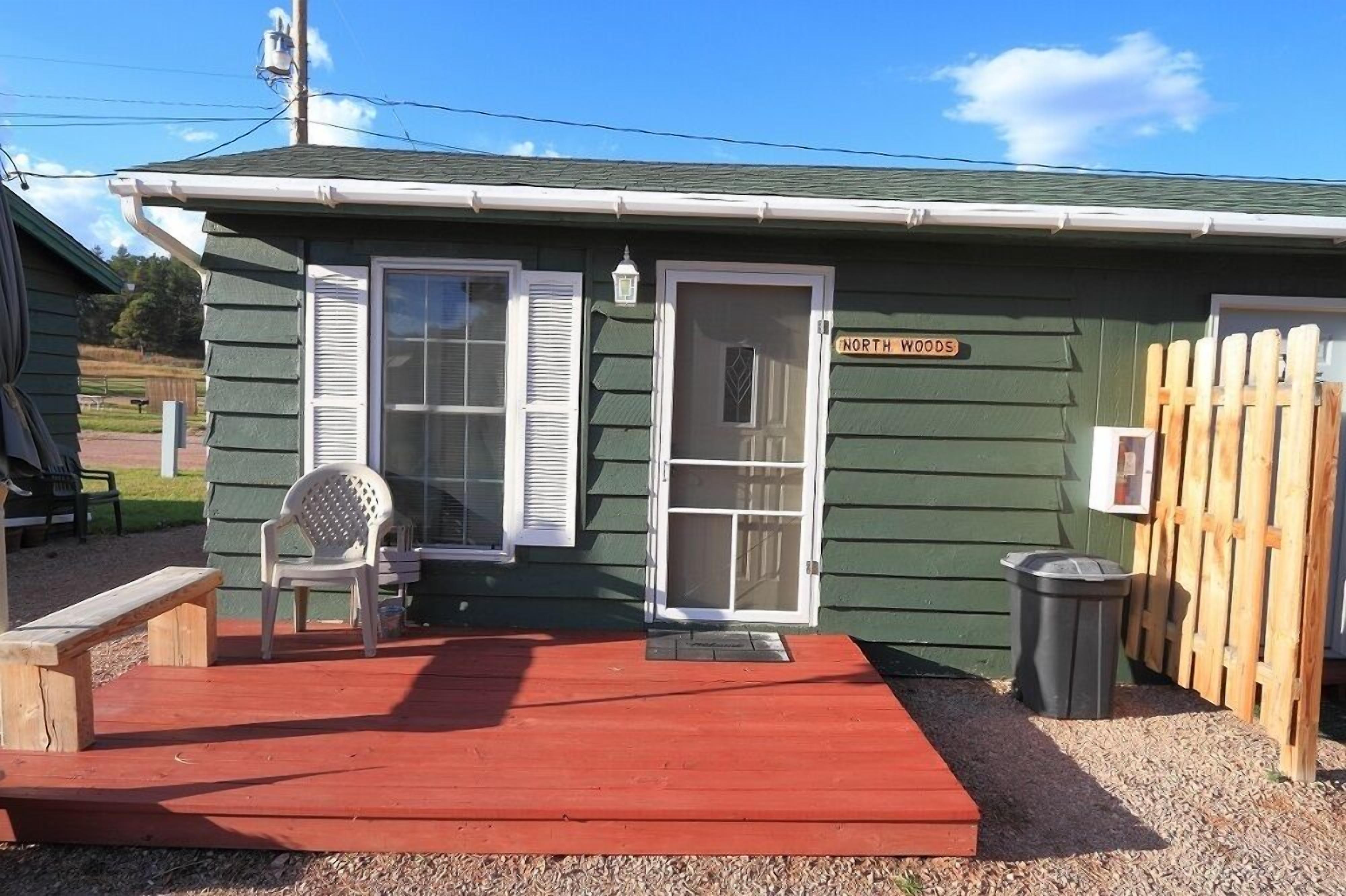 A small, single-story building with a green exterior and a red porch. There is a sign on the building that reads "NORTH WOODS."