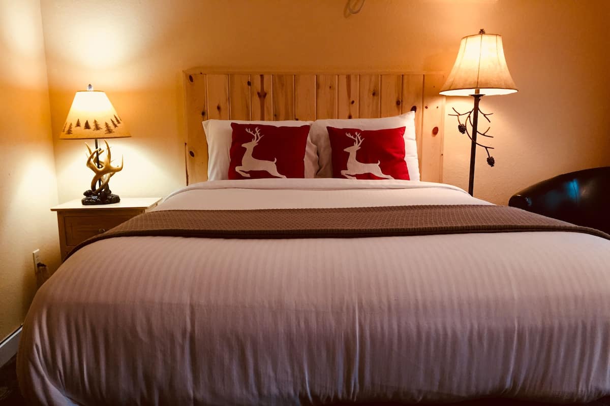 Een net opgemaakt bed met een houten hoofdbord, twee bedlampjes en een decoratief kussen met hertmotief.