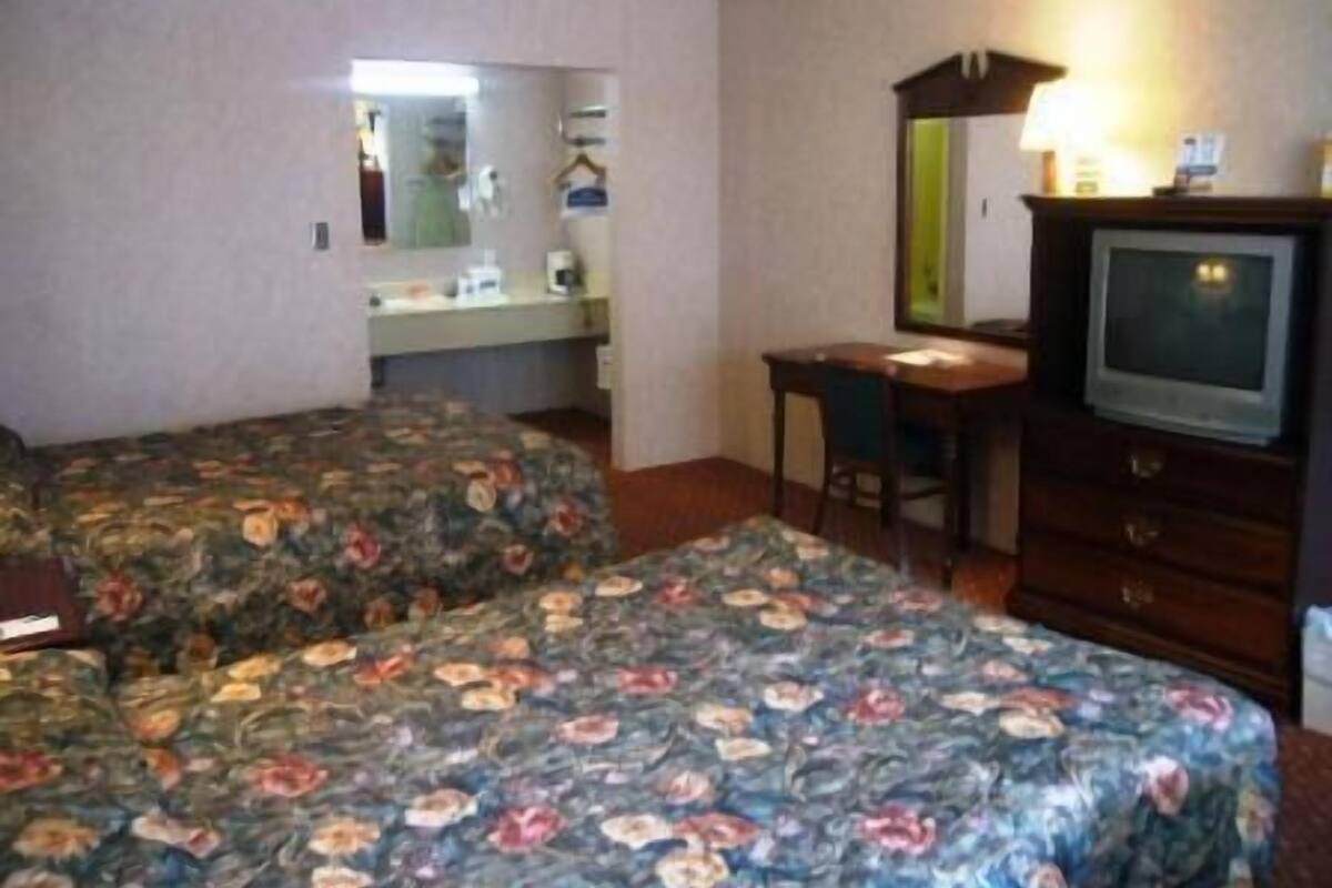 A hotel room with two beds, a desk, a dresser, a television, and a mirror.