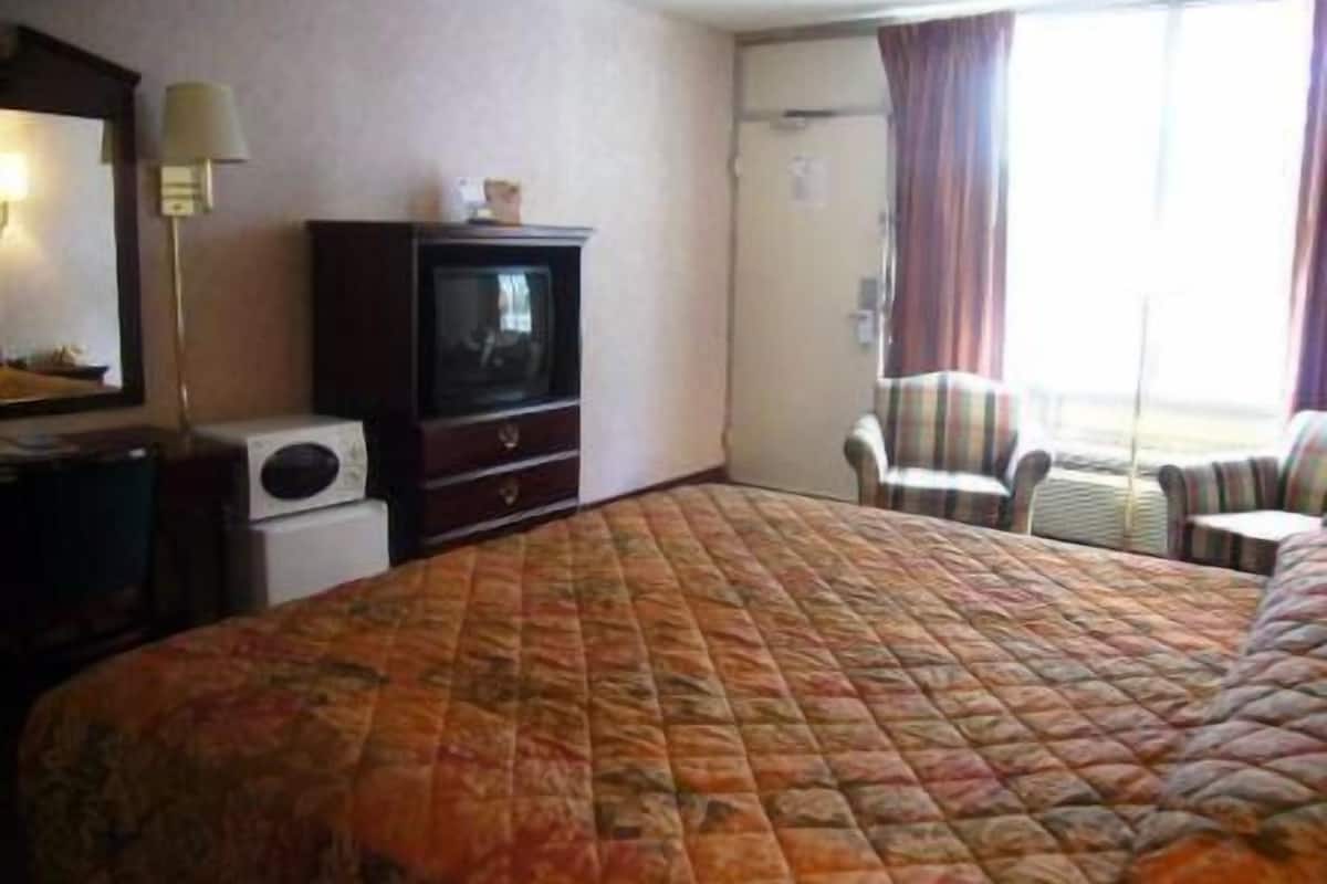 A hotel room with a large bed, a television on a dresser, a chair, and a window with curtains.
