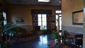 A lobby with a patterned carpet, a sofa, a chair, a table, and potted plants. - Travel Inn (Birmingham)