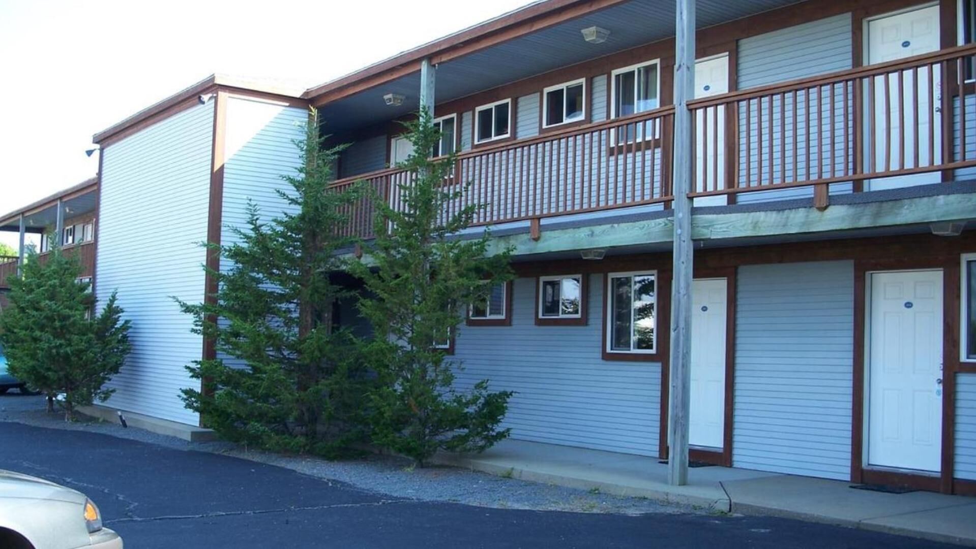 A two-story motel with a balcony on the upper floor, a garage door on the ground floor, and a parking lot in front.