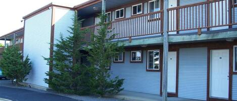 A two-story motel with a balcony on the upper floor, a garage door on the ground floor, and a parking lot in front.