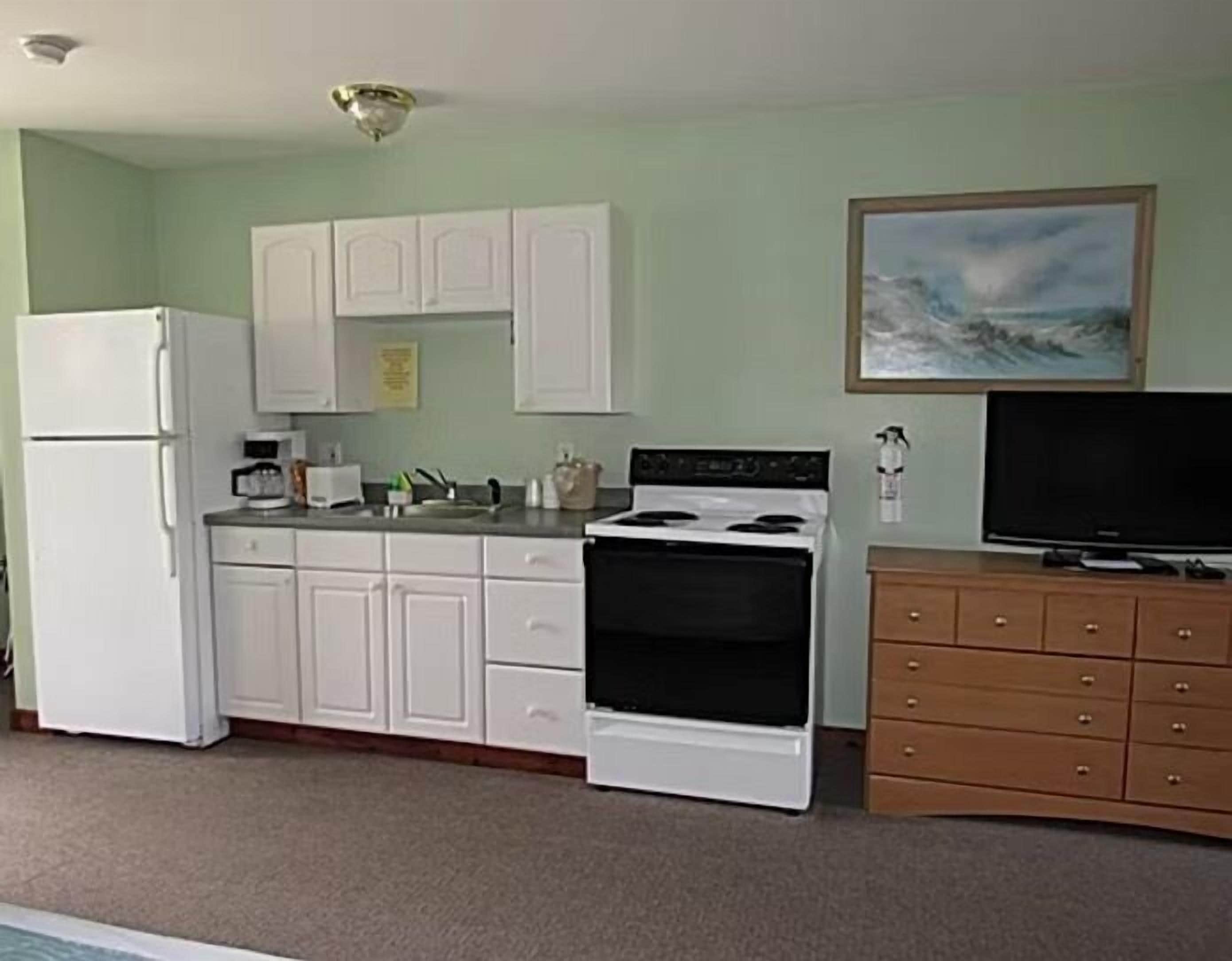 A compact kitchen with white cabinets, a stove, a refrigerator, and a wooden cabinet with drawers.