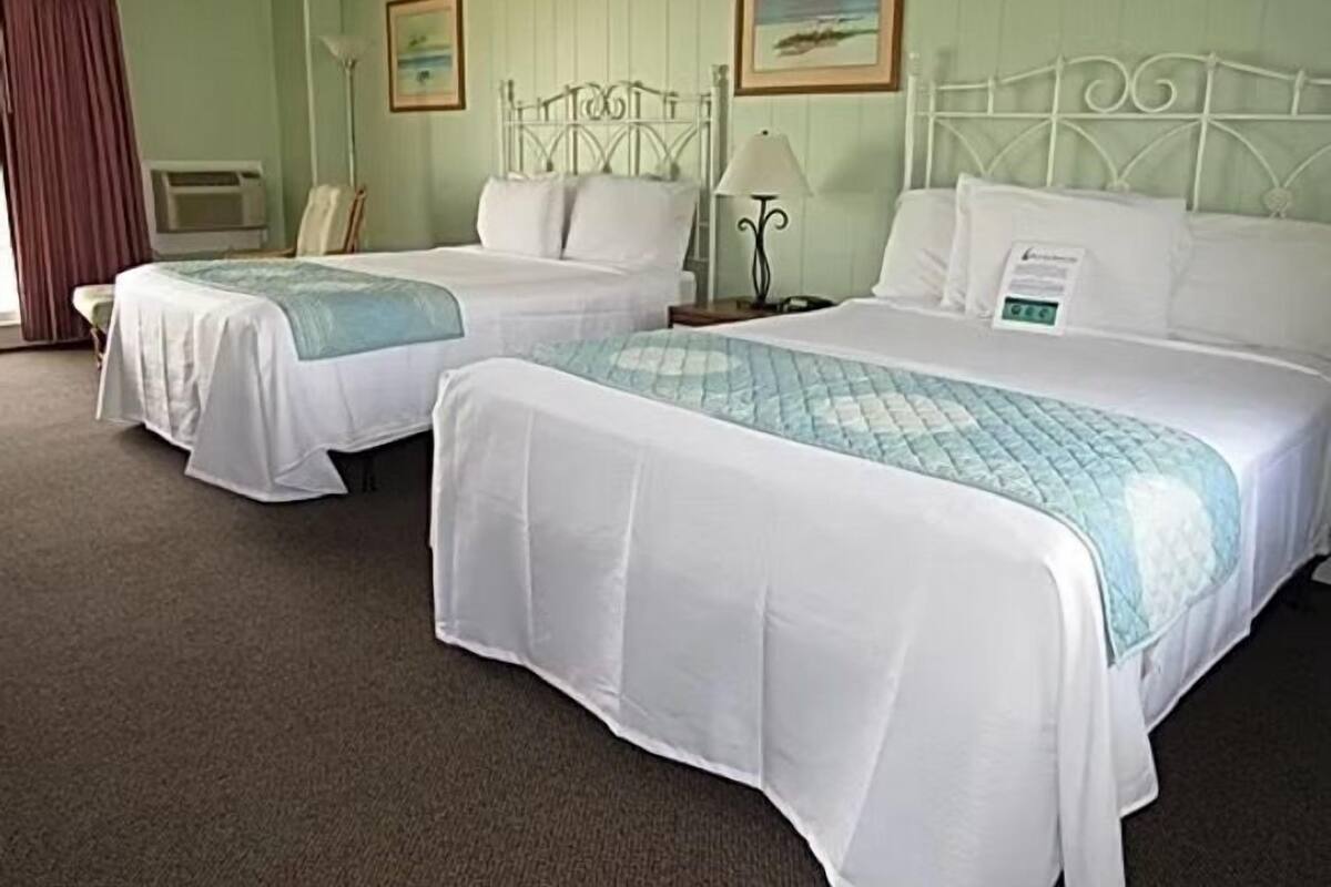 Een hotelkamer met twee bedden, een bureau, een lamp en twee ingelijste foto's aan de muur.