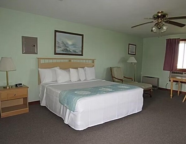 A hotel room with a bed, a desk, a chair, a lamp, and a ceiling fan.