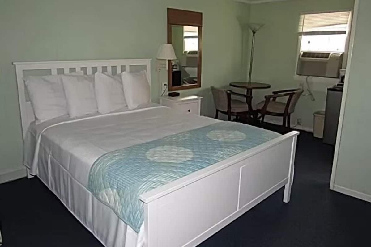 Een keurig opgemaakt slaapkamer met een bed, nachtkastje, lamp, stoel en een kleine tafel met een lamp.