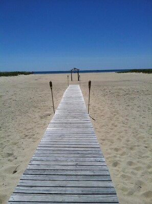 A wooden pier leading to a beach with a clear sky.