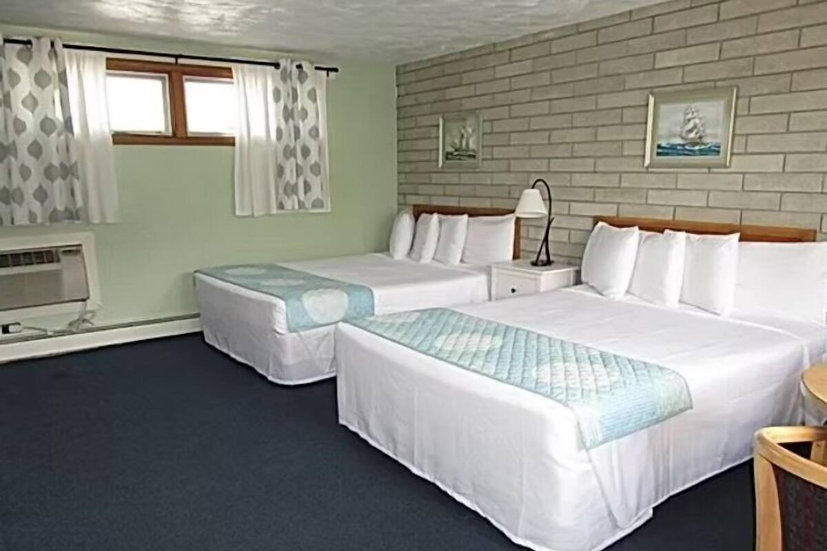 Een hotelkamer met twee bedden, een bakstenen muur, een raam met gordijnen en een klein nachtkastje met een lamp.