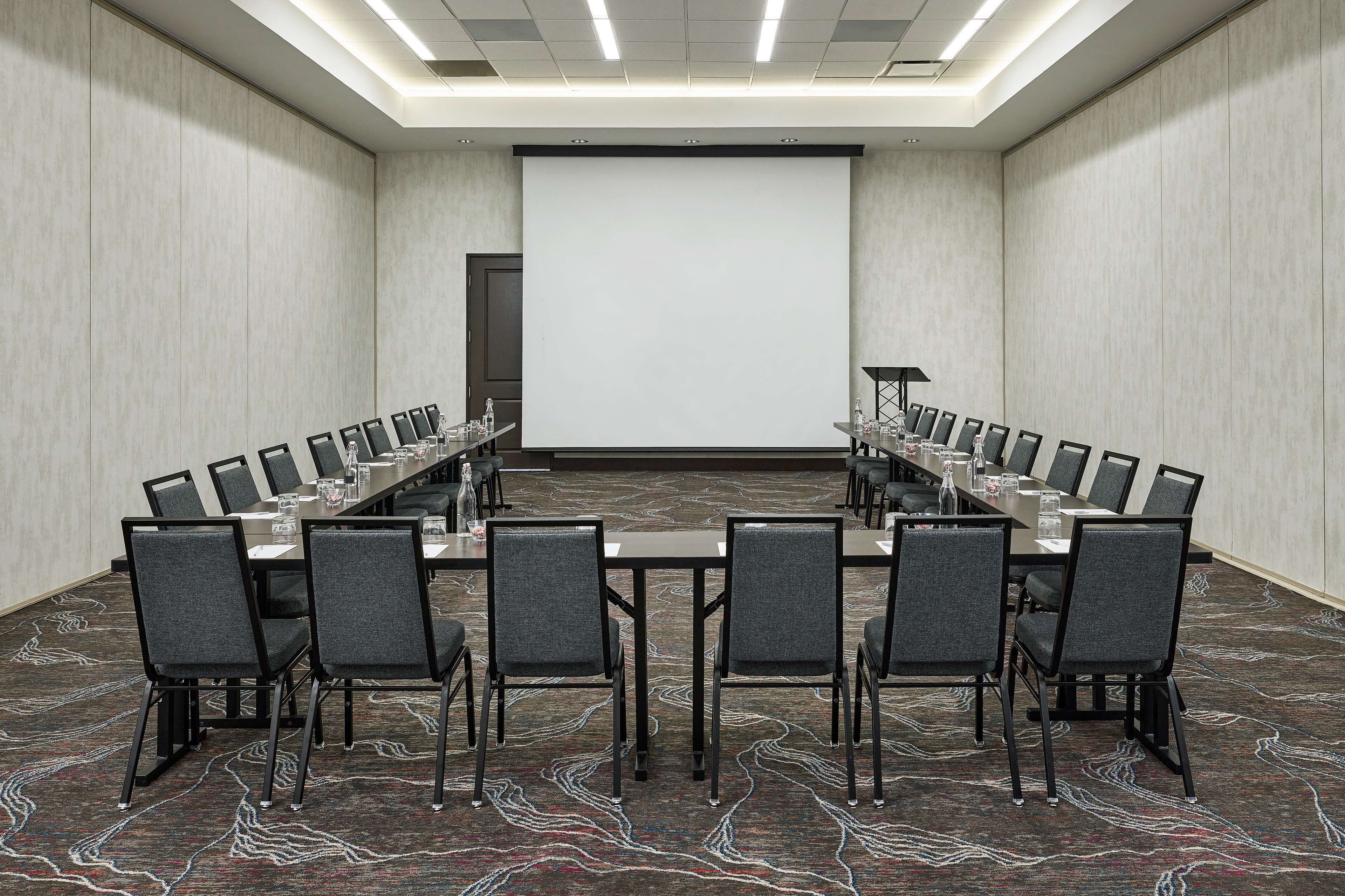 Ein Konferenzraum mit langem Tisch, Stühlen, einer Projektionsleinwand und Teppichboden.