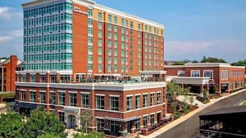 Un hotel de varios pisos con un llamativo letrero de Hilton Garden Inn, que presenta una fachada de ladrillo y vidrio, zonas de estar al aire libre y un patio ajardinado.