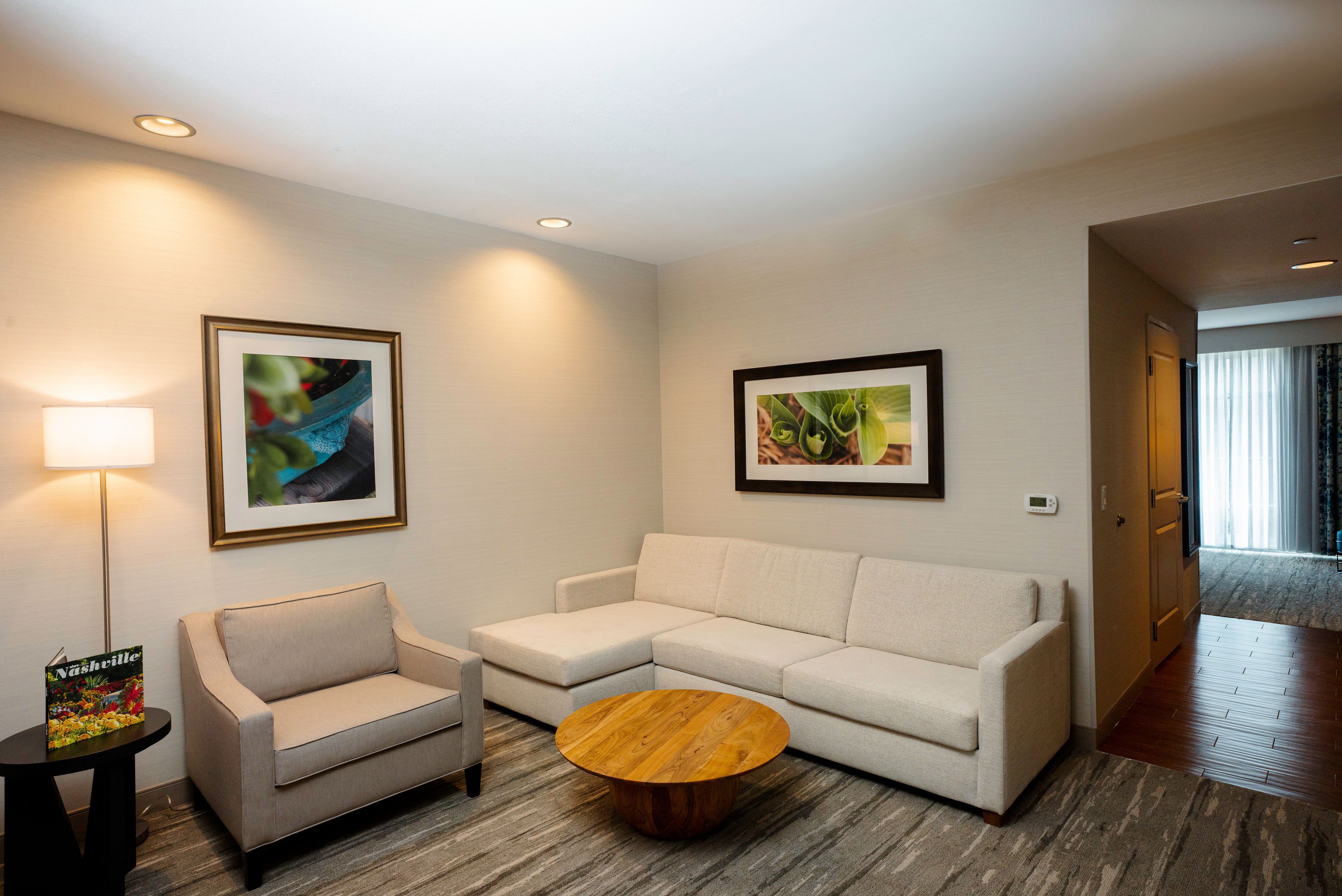 A modern living room with a beige sofa, a round wooden coffee table, and two framed abstract paintings.