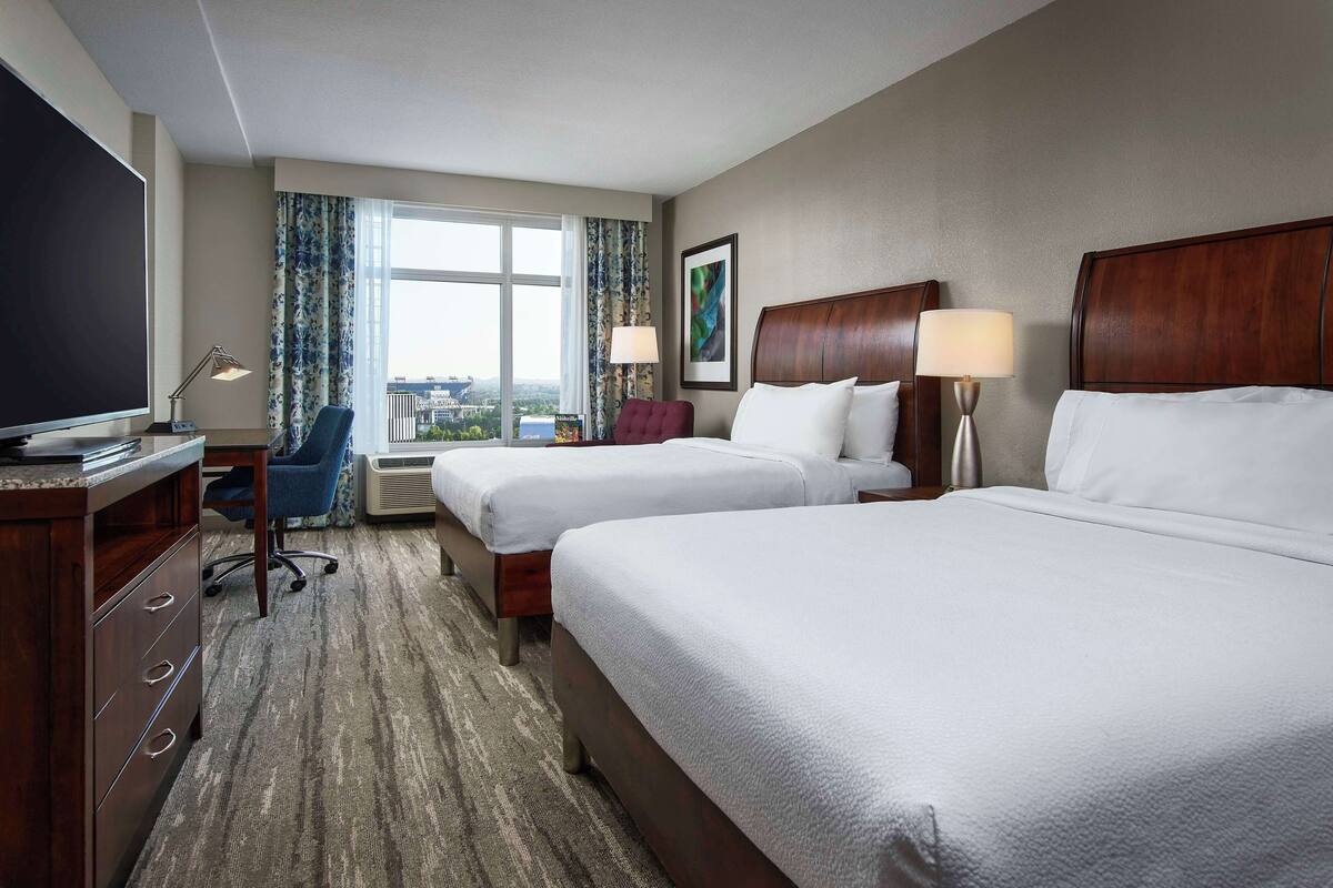 A hotel room with two beds, a desk with a television, and a window with curtains.