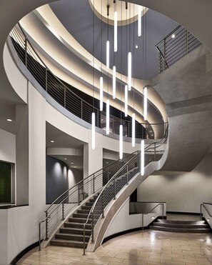 Un interior moderno con una escalera curva, barandillas metálicas y lámparas colgantes.