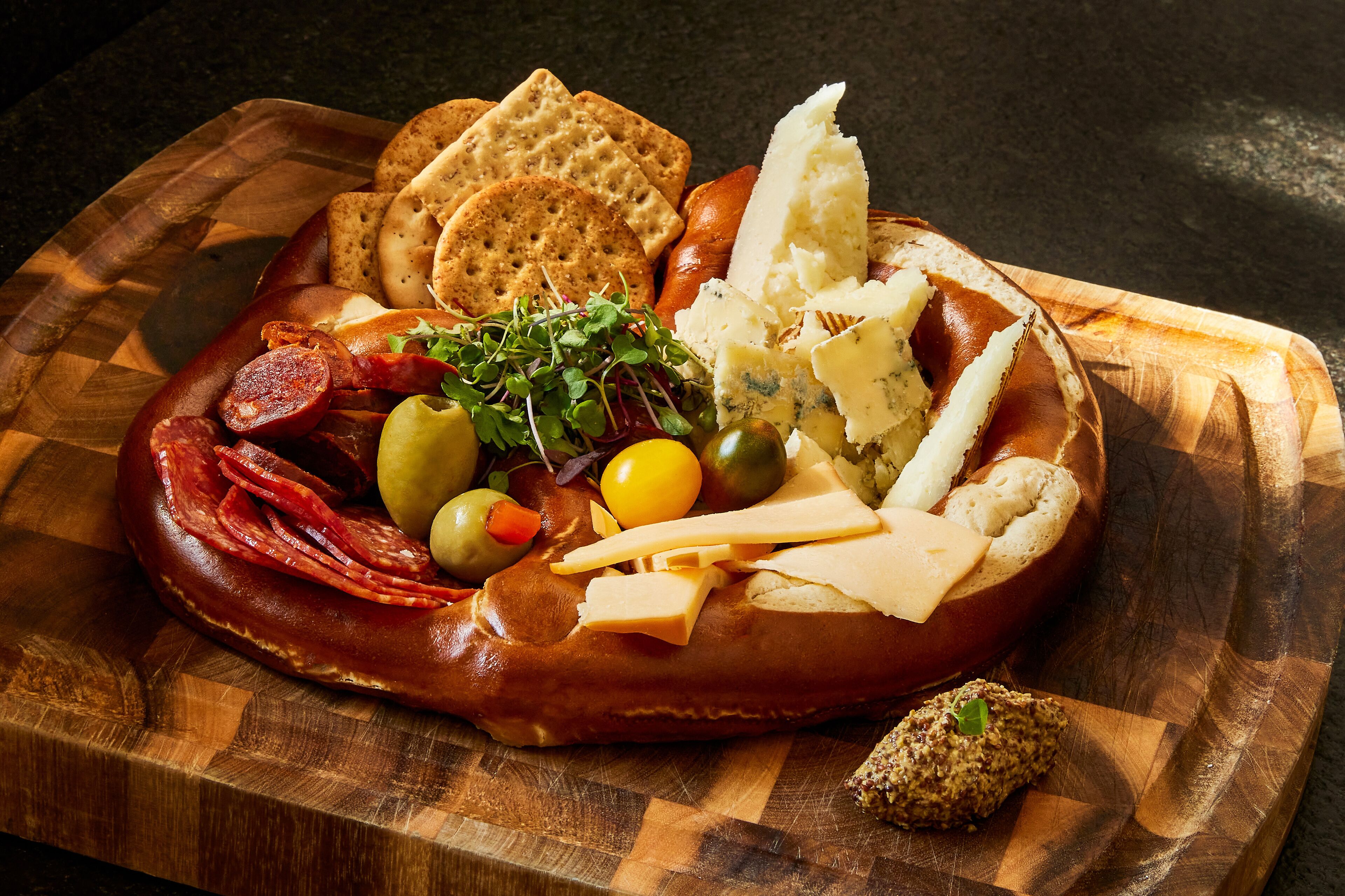Una tabla de fiambres con diversos embutidos, quesos, aceitunas y galletas sobre una tabla de madera.