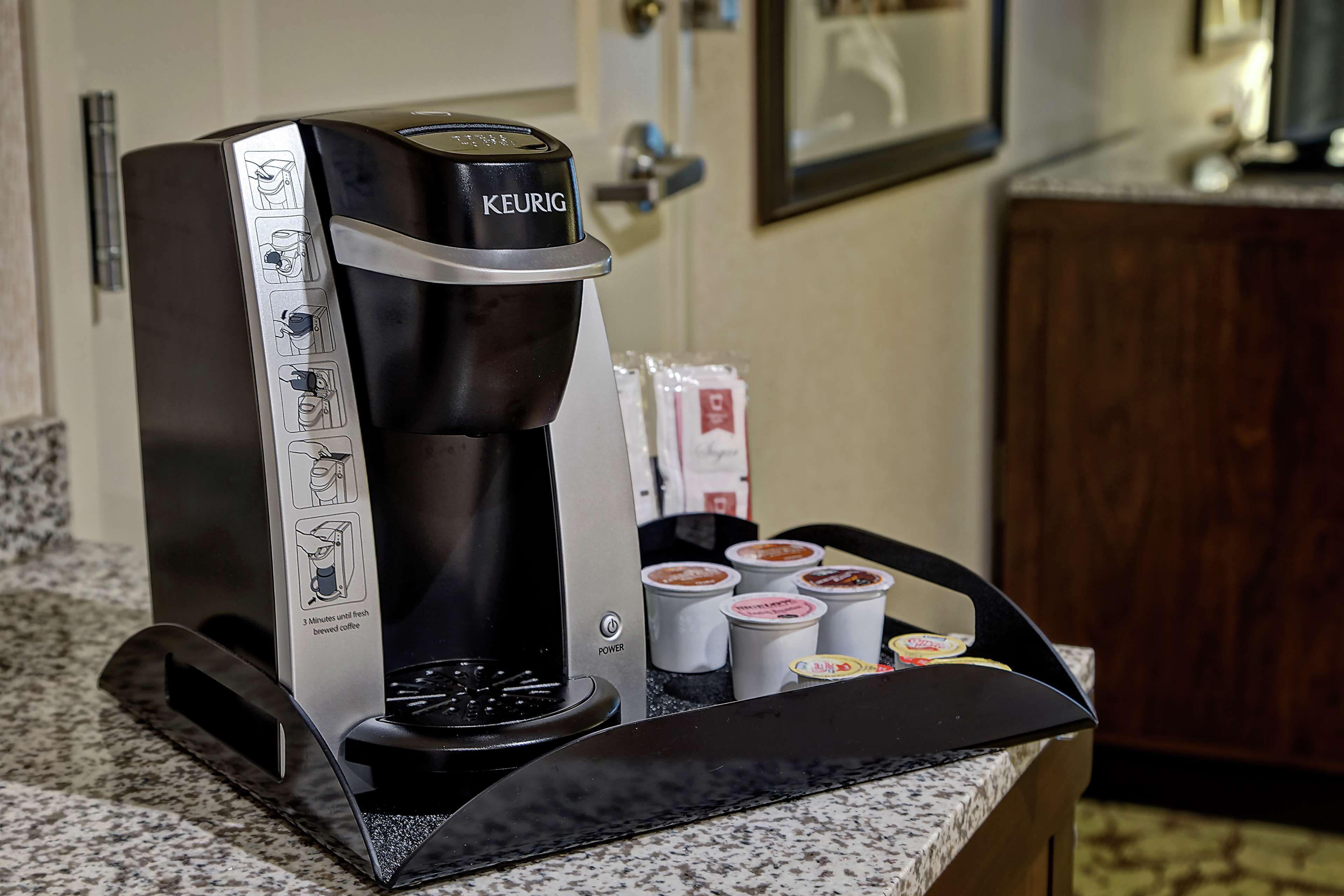 A Keurig coffee maker with a drip tray and several coffee pods on a granite countertop.