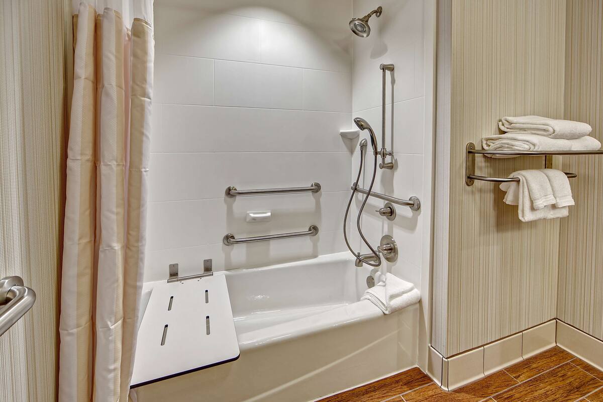 A modern bathroom with a white bathtub, grab bars, a towel rack, and a showerhead.