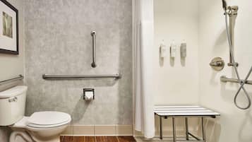 Un baño con inodoro, ducha con cabezal de ducha manual, barras de apoyo y una mesita.